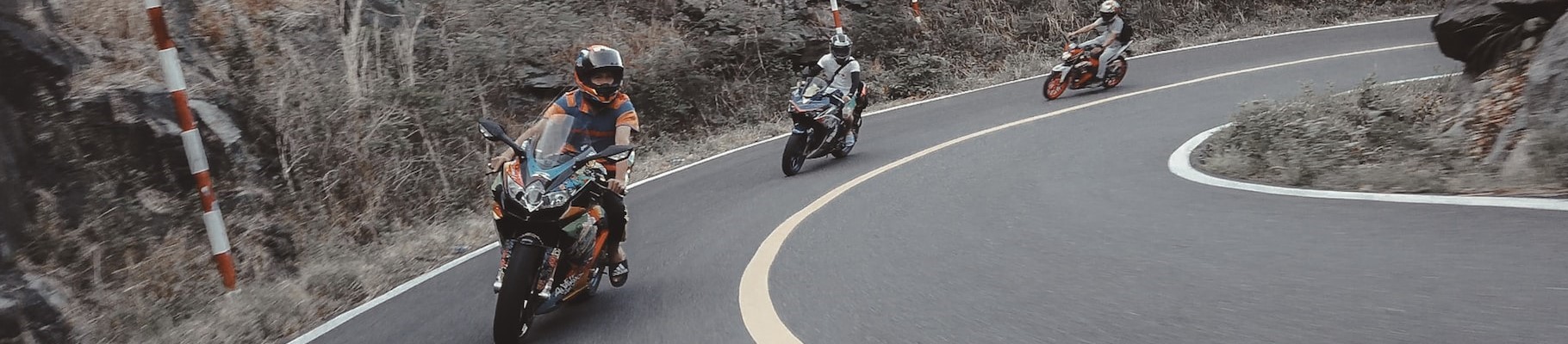 motorcylces riding around a curve in the forest